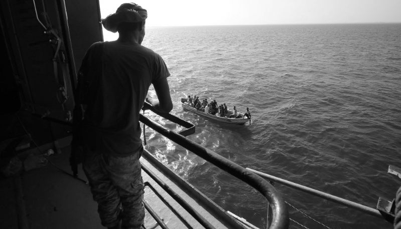 A boat carries people as a Houthi fighter stands guard on the deck of the Galaxy Leader cargo ship, seized by the Houthis off the port of Al-Salif on the Red Sea in Hodeidah province, Yemen, on 5 December 2023.